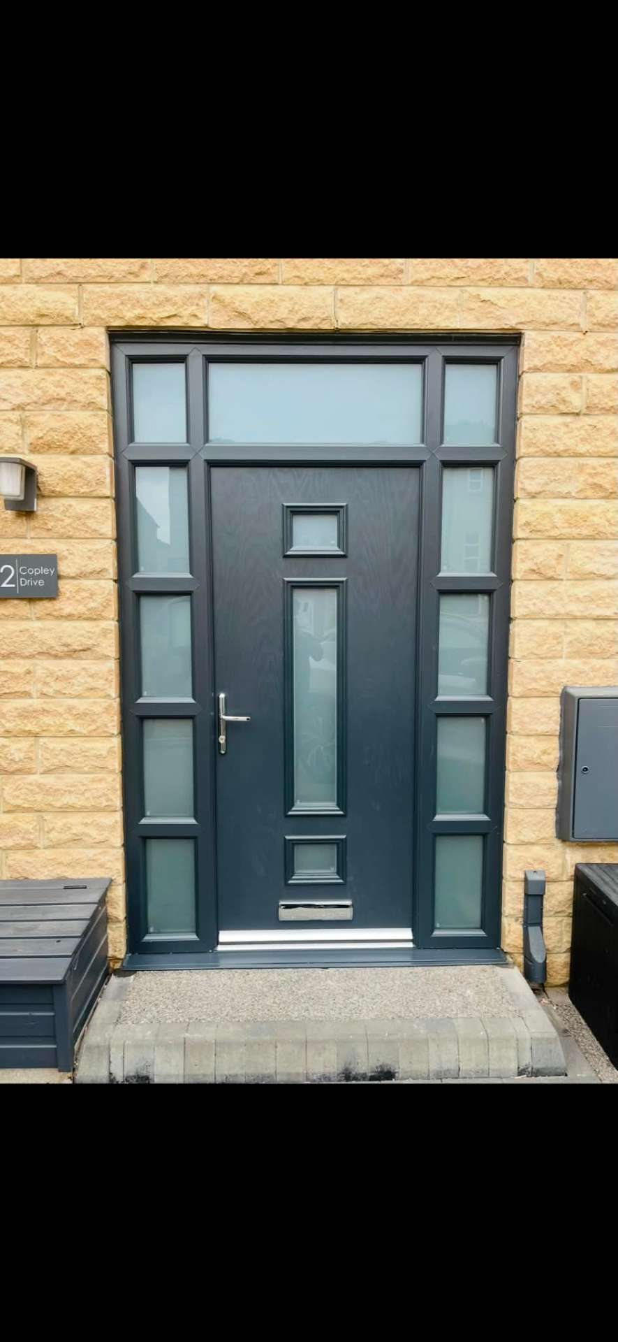 Anthracite grey composite front door with side panels and top light in a stone surround