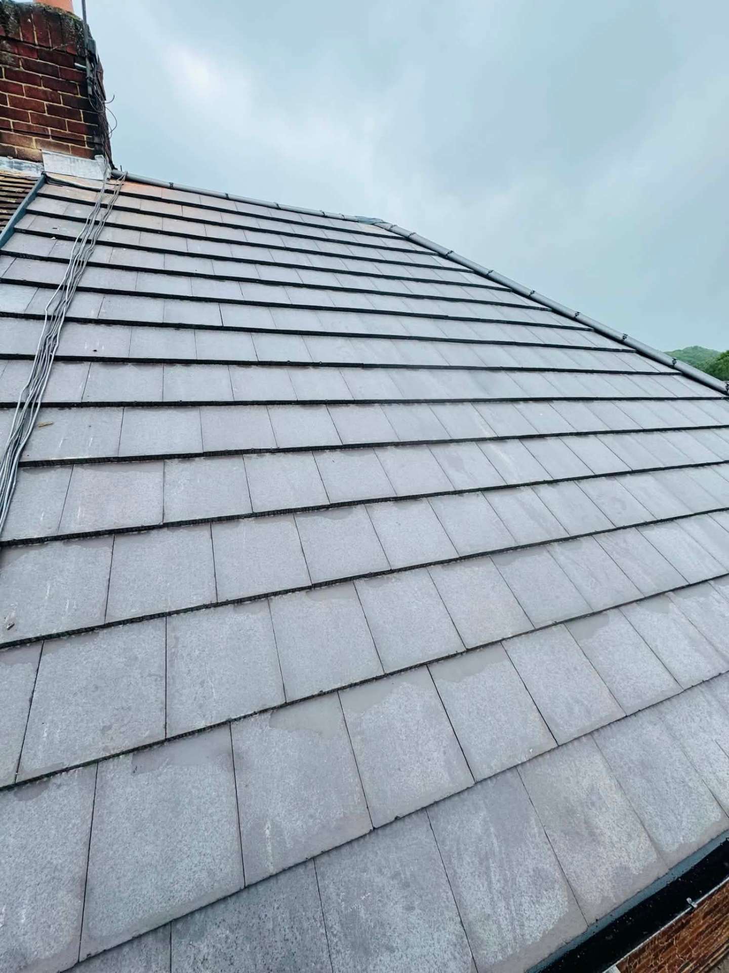 Neatly laid grey roof tiles running up to a repointed chimney stack