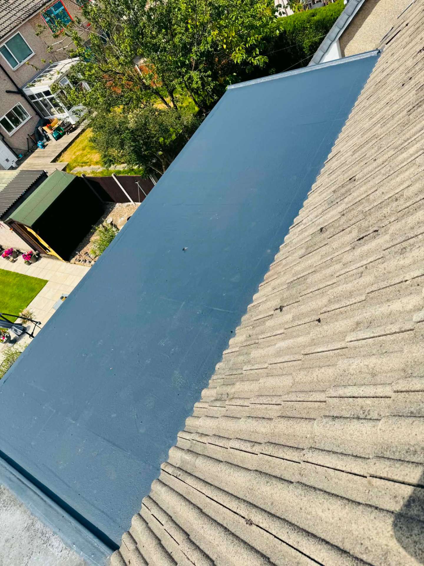 Completed grey fibreglass flat roof with trimmed edge detail alongside a tiled pitched roof