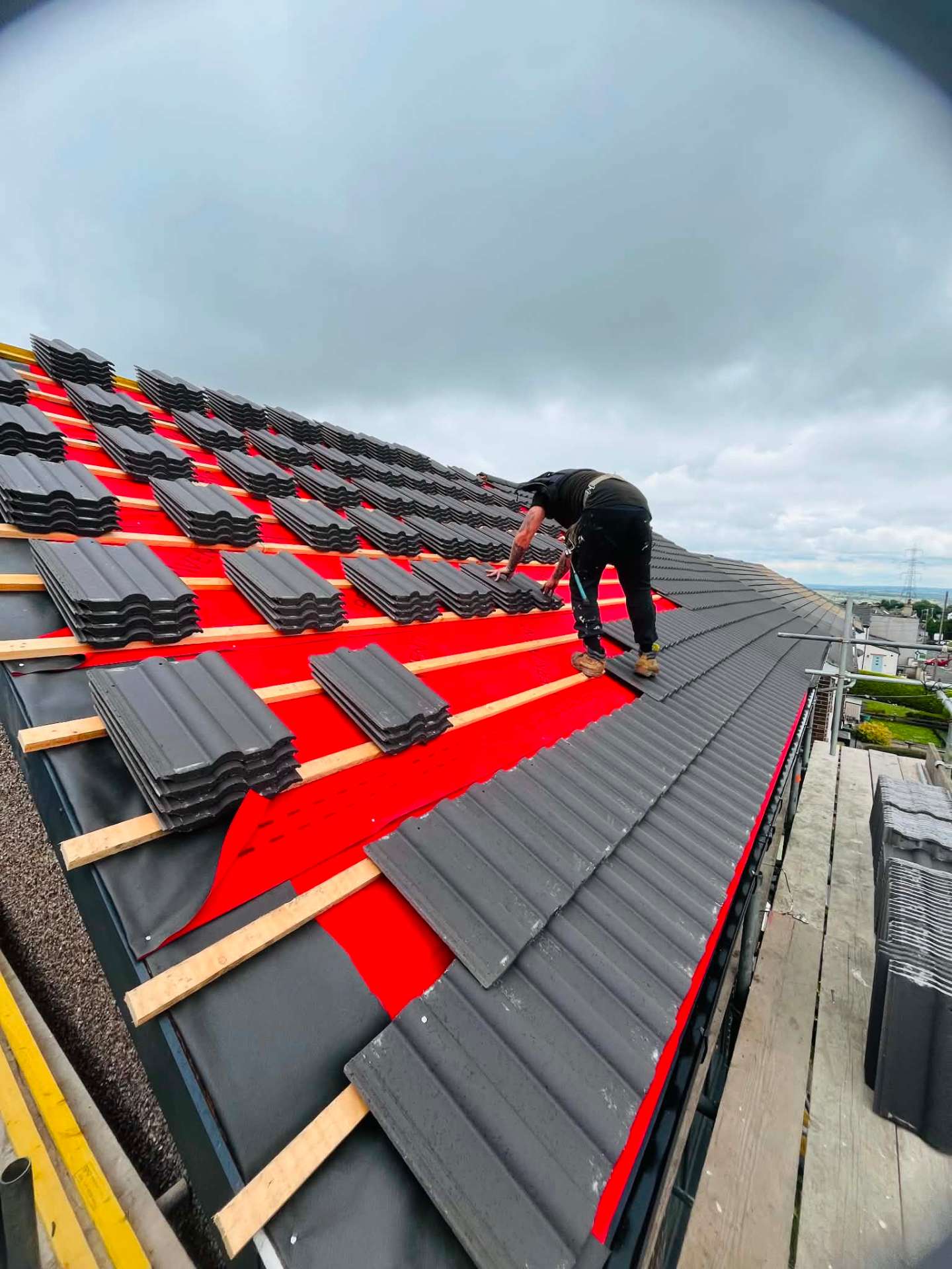 Roofer laying new grey concrete tiles over breathable membrane and battens on a hipped roof