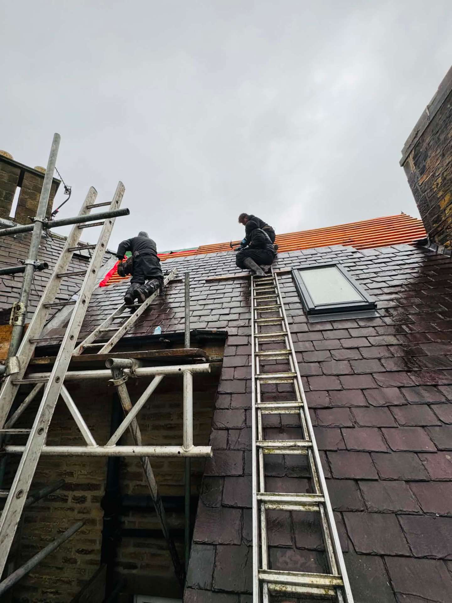 D&M Roofing team working on a slate roof, stripping and re-battening a damaged section
