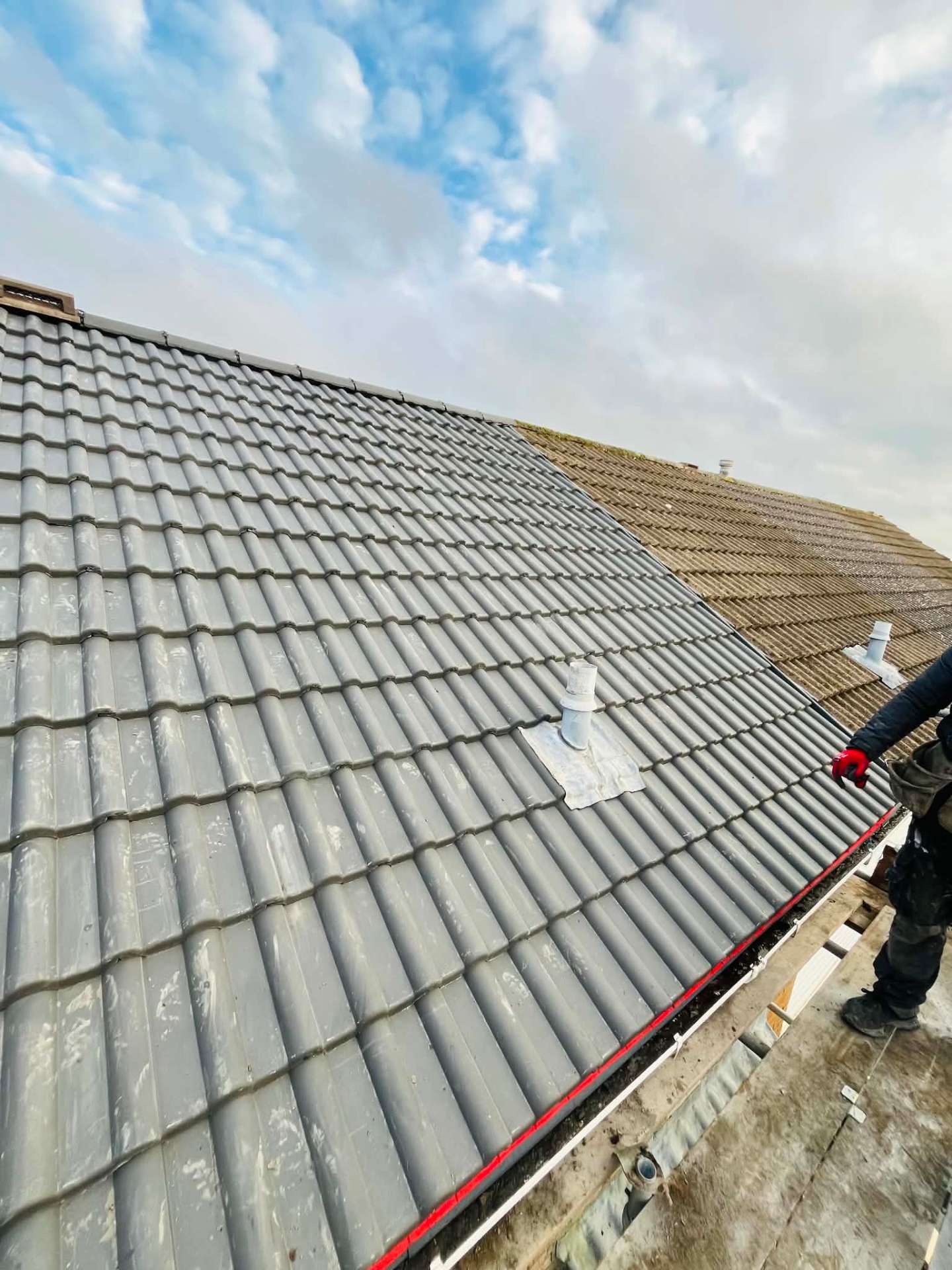 Roof part way through re-tiling, new grey tiles on one side and the old weathered covering on the other